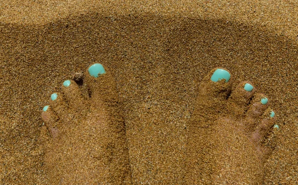 female feet with turquoise polish on bright yellow sand