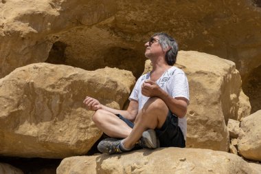 Matala 'da sarı bir kayanın üzerinde yoga pozu veren bir adam oturuyor.