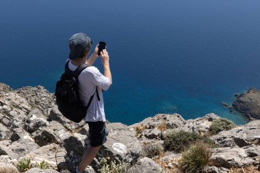 Denizin, Yunanistan 'ın, Girit' in kıyısındaki sarp kayalıklarda fotoğraf çeken adam.