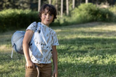A boy with a bag stands on the edge of the forest. High quality photo