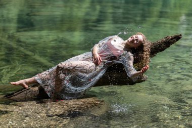 A young model plays with splashes on a mountain lake against the background of crystal clear transparent water. High quality photo