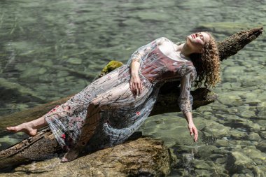 A young model poses on a mountain lake against the backdrop of crystal clear transparent water. High quality photo