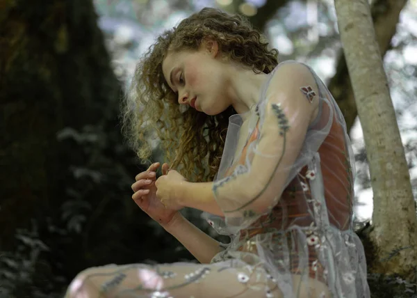 Beautiful girl with long curly hair sits on a tree. High quality photo