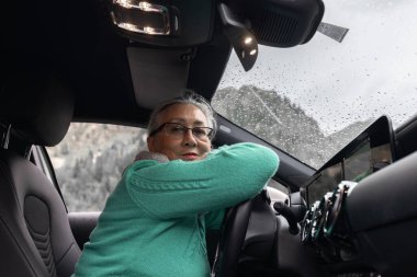 Gri saçlı bir bayan sürücü koltuğuna oturur ve direksiyona sarılır. Yüksek kalite fotoğraf