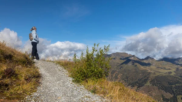 A gray-haired woman stands on a mountain road and looks at a beautiful landscape in the Austrian Alps. High quality photo