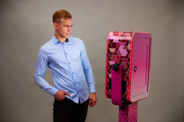 Erkek, açık hava DSLR fotoğraf kabininin önünde poz veriyor. Gri arka planda mavi bir gömlek giyiyor..