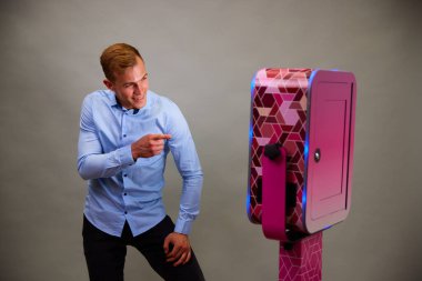 Erkek, açık hava DSLR fotoğraf kabininin önünde poz veriyor. Gri arka planda mavi bir gömlek giyiyor..