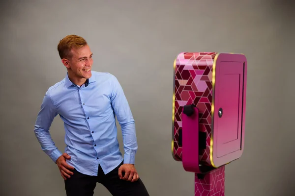 Erkek, açık hava DSLR fotoğraf kabininin önünde poz veriyor. Gri arka planda mavi bir gömlek giyiyor..