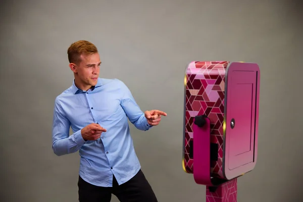 Erkek, açık hava DSLR fotoğraf kabininin önünde poz veriyor. Gri arka planda mavi bir gömlek giyiyor..