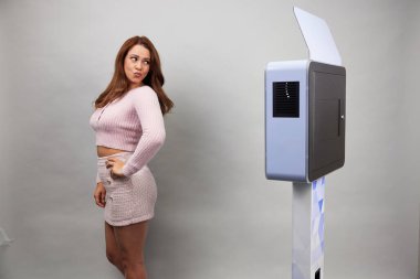 Beyaz bir fotoğraf kabininin önünde poz veren kadın.