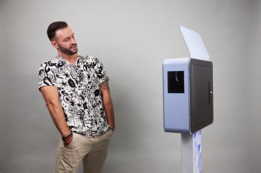 Erkek beyaz bir fotoğraf kabininin önünde poz veriyor.