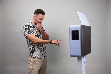 Erkek beyaz bir fotoğraf kabininin önünde poz veriyor.