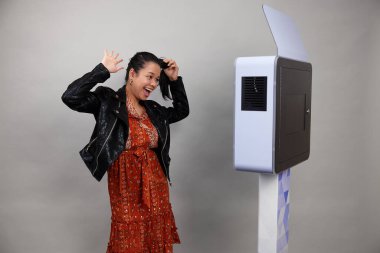 Beyaz bir fotoğraf kabininin önünde poz veren kadın.