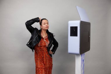 Beyaz bir fotoğraf kabininin önünde poz veren kadın.