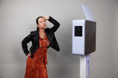 Beyaz bir fotoğraf kabininin önünde poz veren kadın.