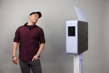 Erkek beyaz bir fotoğraf kabininin önünde poz veriyor.