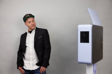 Erkek beyaz bir fotoğraf kabininin önünde poz veriyor.