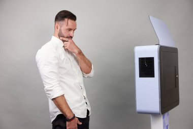 Erkek beyaz bir fotoğraf kabininin önünde poz veriyor.