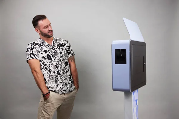 Erkek beyaz bir fotoğraf kabininin önünde poz veriyor.