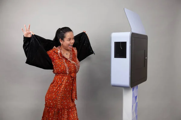 Beyaz bir fotoğraf kabininin önünde poz veren kadın.