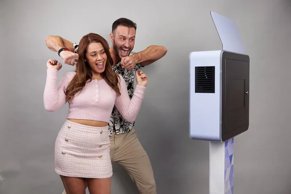 Beyaz bir fotoğraf kabininin önünde poz veren erkek ve kadın.