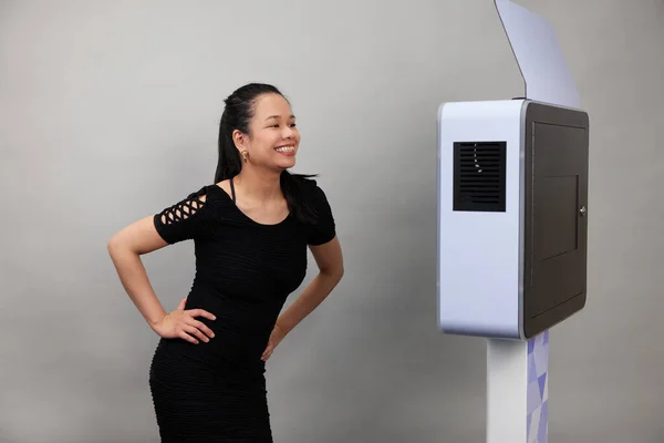 Beyaz bir fotoğraf kabininin önünde poz veren kadın.