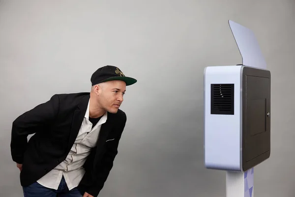 Erkek beyaz bir fotoğraf kabininin önünde poz veriyor.