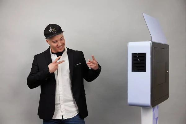 Erkek beyaz bir fotoğraf kabininin önünde poz veriyor.