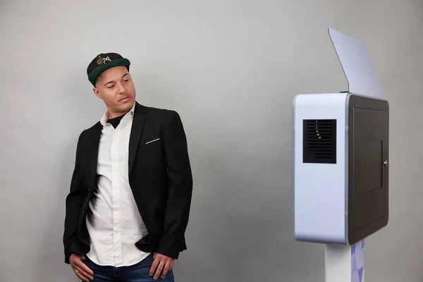 Erkek beyaz bir fotoğraf kabininin önünde poz veriyor.