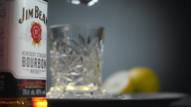 WARSAW, POLAND - SEPTEMBER 10, 2021: Stor isbit släpps till whisky glas i slow motion med flaska Jim Beam bourbon i bakgrunden, Full HD Prores HQ 240 fps — Stockvideo