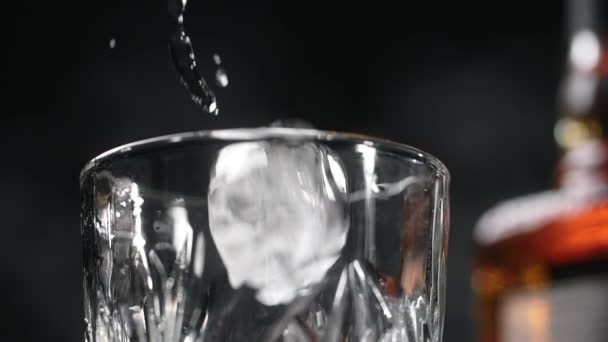 Cubos de hielo se están cayendo al vaso en cámara lenta con la botella de bebida alcohólica en el fondo, Full HD Prores HQ 240 fps — Vídeo de stock