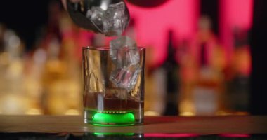 Barmen bardağa yeşil ışıkta yavaş çekimde buz küpleri ekliyor. Bu da kokteyli bar tezgahındaki 4k Prores 120 fp yapıyor.