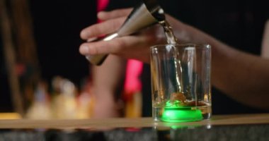 Barmen jigger 'dan bardağa kadar alkolün bir kısmını ağır çekimde yeşil ışıkla doldurur, bu da kokteyli bar tezgahında, 4k Prores 120 fps yapar.