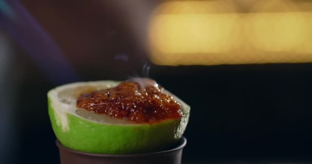 Barman fond le sucre de canne en morceaux avec des gouttes de grenadine dedans avec brûleur à gaz sur la moitié de la chaux, 4k 120 fps Prores HQ — Video