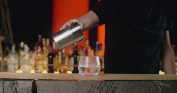 Бармен наливает смешанный коктейль из шейкера в кубик льда на коктейль стекло в замедленной съемке, бармен делает коктейль со льдом и смешанными алкогольными напитками, 4k 120 кадров в секунду Прорес HQ — стоковое видео