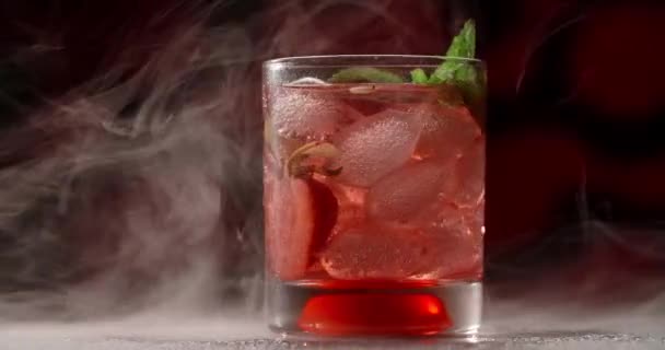 Zimne szkło z czerwonym koktajlem wiruje powoli w dymie na ciemnym tle, napoje alkoholowe i napoje, koktajl bezalkoholowy, wideo obiektu lemoniady, 4k Prores HQ — Wideo stockowe