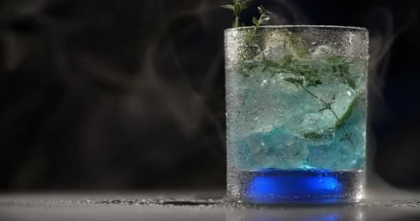 Kaltes Glas mit blauem Cocktail dreht sich langsam im Rauch auf dem dunklen Hintergrund, alkoholische Getränke und Getränke, alkoholfreier Cocktail, Objektvideo von Limonade, 4k Prores HQ — Stockvideo