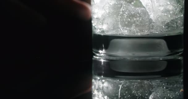 Mans mano toca el vaso con cóctel y la parte inferior de las luces de cristal, cóctel en el fondo negro, bebida fría, cóctel de refresco, 4k Prores HQ 60 fps — Vídeo de stock
