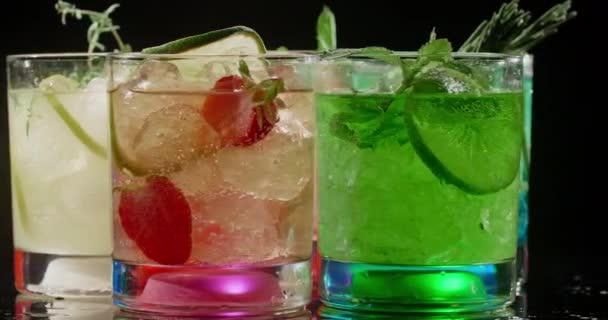 Kalte bunte Cocktails auf schwarzem Hintergrund, aufgehellte Gläser, Erfrischungsgetränke, 4k Prores HQ — Stockvideo