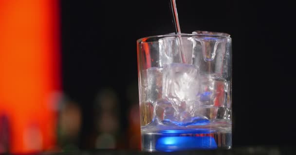 Barman vierte líquido transparente a la copa de cóctel con cubitos de hielo en cámara lenta, haciendo que el cóctel en el mostrador del bar, 4k Prores HQ 120 fps — Vídeo de stock