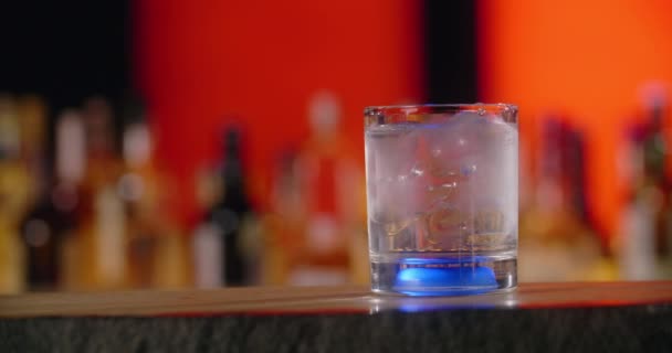 Limoen valt in het cocktailglas met transparante drankjes en ijsblokjes in slow motion, verse koude drank op de bar, 4k 120 fps Prores HQ — Stockvideo