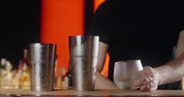 Barmen, dondurulmuş kokteyl bardağına forseps ile büyük buz küpü koyar, bu da kokteyli tezgahta yapar, 4k Prores HQ.
