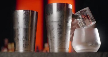 Barmen, dondurulmuş kokteyl bardağına forseps ile büyük buz küpü koyar, bu da kokteyli tezgahta yapar, 4k Prores HQ.