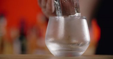 Barmen, dondurulmuş kokteyl bardağına forseps ile büyük buz küpü koyar, bu da kokteyli tezgahta yapar, 4k Prores HQ.