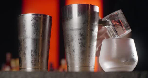 Barmen, dondurulmuş kokteyl bardağına forseps ile büyük buz küpü koyar, bu da kokteyli tezgahta yapar, 4k Prores HQ. — Stok video