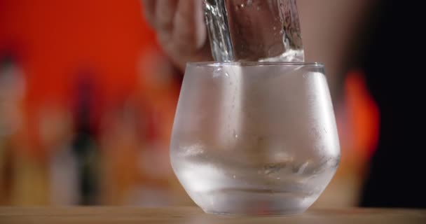 Barkeeper legt große Eiswürfel mit einer Pinzette auf das gefrorene Cocktailglas, wodurch der Cocktail auf der Theke entsteht, 4k Prores HQ — Stockvideo