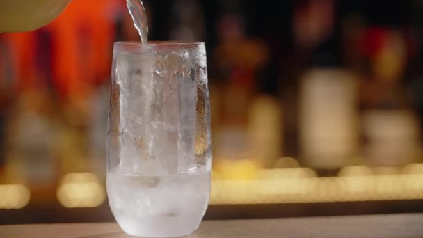 Limonáda se ve zpomaleném záběru nalévá na kostku ledu v koktejlovém skle na barovém pultu, HQ Prores Full HD 240fps — Stock video