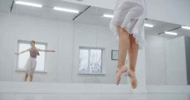 Ballerina in puntschoenen springt meerdere malen in slow motion voor de spiegelwand van de danszaal, danseres springt en doet twine in de lucht, acrobatische dans, 4k 120fps Prores HQ 10 bit — Stockvideo