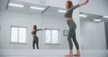 Jimnastikçi, beyaz salonun ayna duvarının önüne atlıyor. Beyaz salonda jimnastik, yoga ve pilates eğitmeni, 4k 120p Prores HQ.