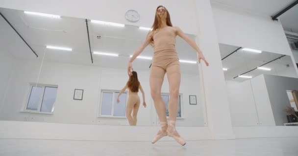 Женщина в пуантах прыгает несколько раз в замедленной съемке перед зеркальной стеной танцевальной комнаты, танцовщица с прыжками и делает бечевку в воздухе, акробатический танец, 4k 120fps Prores HQ 10 бит — стоковое видео